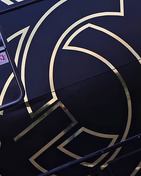 Close-up of the gold GC emblem on the black side of the bus
